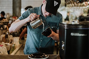Male cafe employee carefully pouring a coffee drink